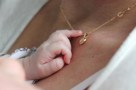 Babyhand greift sanft nach einer goldenen Halskette mit Anhänger auf der Haut einer Person.